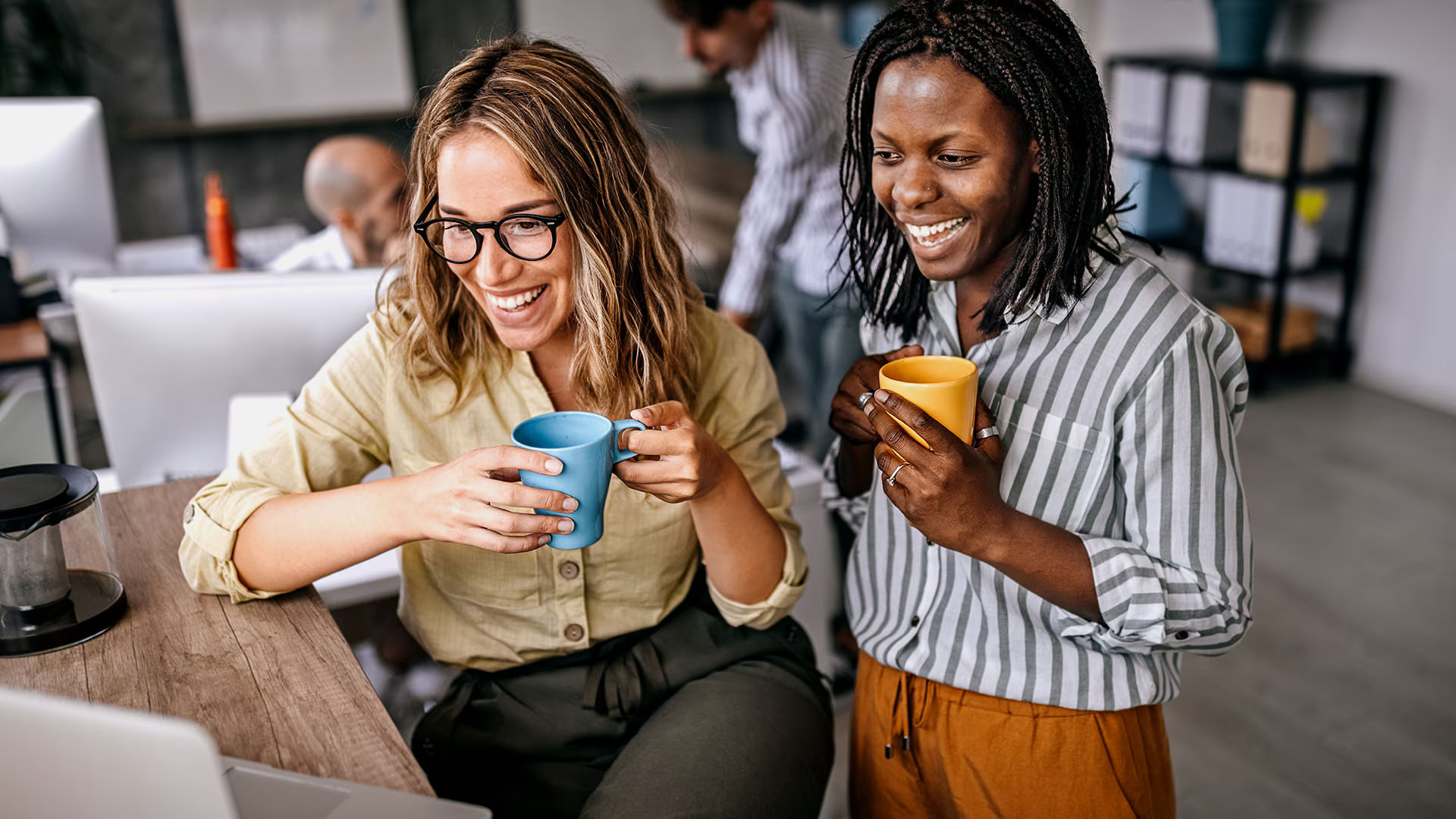 two-coworkers-laughing-drinking-coffee